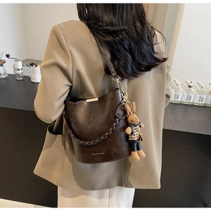 Detail of dark brown leather bucket bag with braided handle and cute rabbit charm
