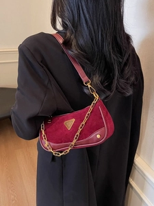 Sac bandoulière tendance en daim bordeaux avec chaîne dorée porté par un mannequin