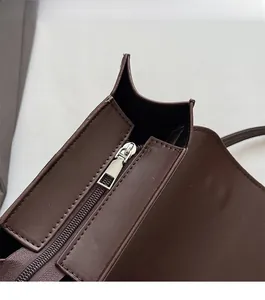 Close-up of smooth silver zipper and matte dark brown leather stitching on handbag