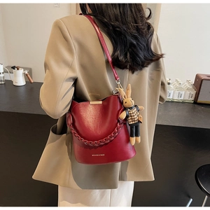 Detail of burgundy leather bucket bag with braided handle and cute rabbit charm on a model