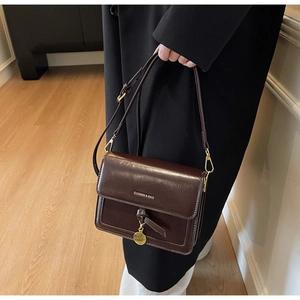 Détail du sac à bandoulière en similicuir marron foncé avec accessoires dorés par un mannequin
