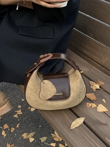 Chic crescent khaki suede and brown leather handbag on wooden bench with autumn leaves
