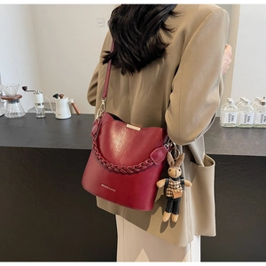 Detail of dark red bucket bag with woven handle, crossbody strap and cute rabbit pendant