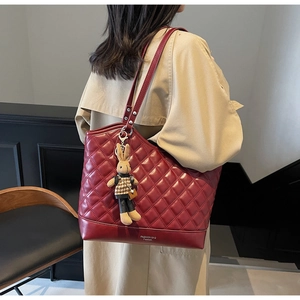 Detail view of burgundy quilted tote bag with rabbit charm and fashion branding