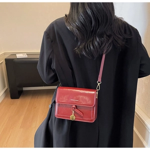 Détail d'un sac bandoulière rouge brillant avec pendentif porté par un mannequin