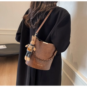 Brown leather bucket bag with woven handle and bunny charm shown on a model