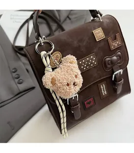 Detail of brown PU leather messenger bag with Good Luck embroidery and plush bear charm