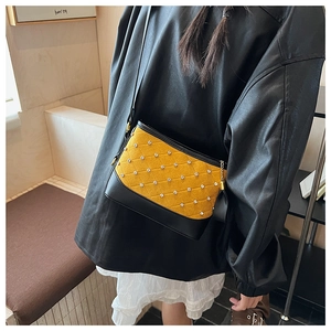 Détail du sac seau matelassé jaune avec clous et breloque pompon sur bandoulière
