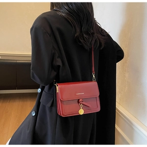 Sac à bandoulière en cuir bordeaux avec détails dorés porté sur un manteau noir