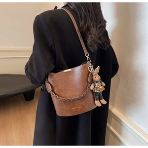 Brown leather bucket bag with woven handle and cute rabbit charm shown on a model