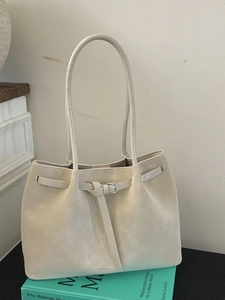 Minimalist cream suede tote bag with metal buckle detail placed on a green book