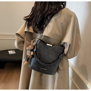 Detail of a black bucket bag with a chain strap and a plaid rabbit charm accessory