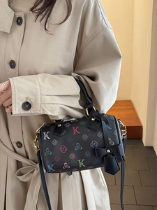 Elegant black barrel bag with floral K pattern and bow charm on a model's shoulder