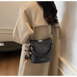 Detail of black matte bucket bag with braided handle and a brown rabbit doll pendant
