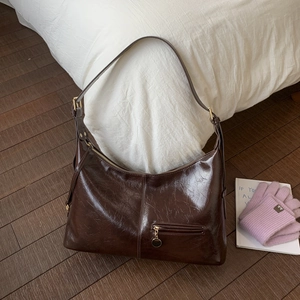 Detail of dark brown oil wax leather hobo bag with gold buckle and smooth glossy finish