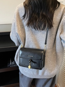 Sac bandoulière chic en cuir noir avec chaîne et breloque dorée sur mannequin
