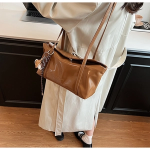 Brown oil wax leather tote bag shown with an elegant fuzzy charm on a tan trench coat