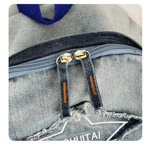Detailed macro view of light blue denim backpack with double gold metal zippers and star patch
