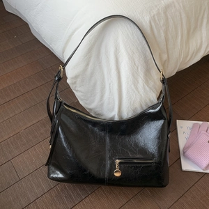 Detail of glossy black patent leather tote with gold zippers and wrinkled texture