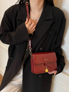 Sac bandoulière rouge foncé tendance avec médaille dorée présenté sur un mannequin