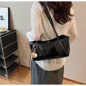 Detail of black glossy faux leather tote with baseball charm on model in modern interior