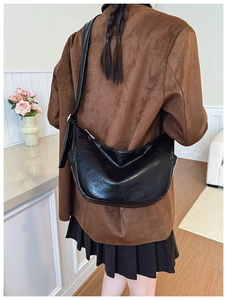 Detail of a black leather crescent crossbody bag worn over a stylish brown suede jacket