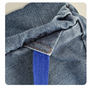 Detail of blue denim backpack showing high-quality orange stitching and durable woven strap