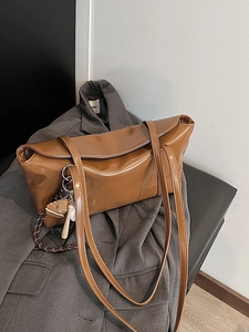 Brown waxed leather tote bag with shoulder straps and baseball charm on grey blazer