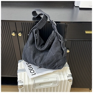 Detail van zwarte denim hobo tas met brede schouderband en zilveren oogjes gespen