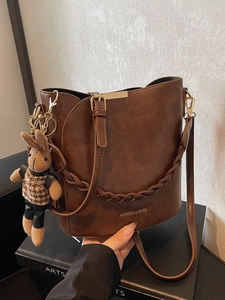 Deep brown bucket bag with woven straps and a rabbit doll pendant for women's daily commute