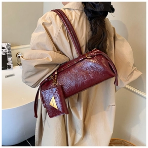Détail d'un sac à bandoulière en cuir verni bordeaux avec logo doré et texture plissée