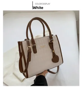 Detail of white quilted crossbody bag with brown leather handles and heart pendant
