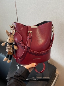 Deep red leather bucket bag with woven handle, shoulder strap and plush rabbit charm