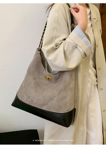 Model wearing a grey suede tote bag with diamond stitching and golden chain strap