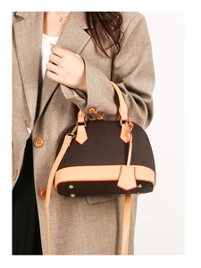 Détail d'un sac à main marron sur blazer, avec bords rouges et pieds en métal doré
