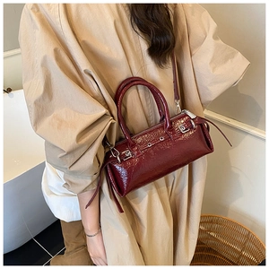 Sac Boston en cuir verni bordeaux avec œillets métalliques et détails de sangle portés