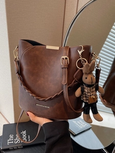 Retro brown bucket bag with woven handle and plush rabbit charm in studio setting