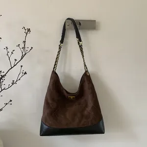 Detail of dark brown suede tote bag featuring quilted diamond pattern and chain straps