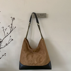 Close-up of brown suede tote bag featuring beige quilted stitching and chain strap