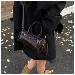 Détail d'un sac tonneau marron foncé brillant avec boucles argentées en style de rue
