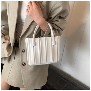 Détail d'un sac seau blanc plissé porté par un mannequin en tailleur gris élégant