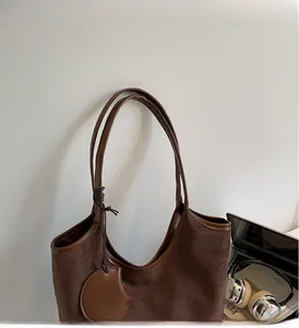 Dettaglio della borsa tote in pelle scamosciata marrone scuro con manici rinforzati e ciondolo a foglia