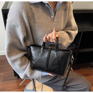 Detail of black glossy tote bag with crinkled texture and silver metal hardware