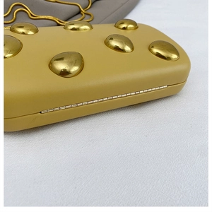 Dettaglio della borsa a mano giallo senape con grandi borchie dorate e catena sottile