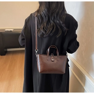 Dark coffee leather tote bag styled on a black coat, showing versatile shoulder carry