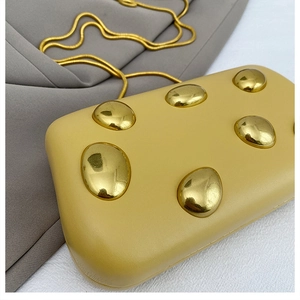 Dettaglio della pochette da sera giallo acceso con borchie dorate e catena