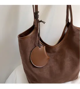 Dettaglio della borsa tote in pelle scamosciata marrone con bordi in pelle e ciondolo