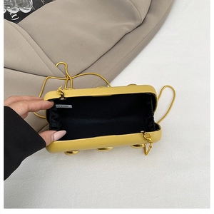 Dettaglio pochette gialla con decoro a semisfera dorata e tracolla a catena