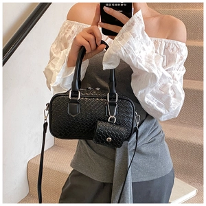 Détail du sac à bandoulière noir tressé avec un mini pendentif porte-monnaie sur l'escalier