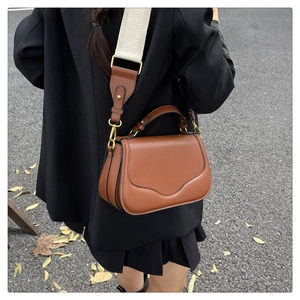 Détails d'un sac besace marron avec large bandoulière en textile et boucles dorées